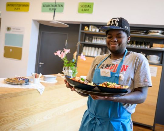 Ein teilnehmer von “besser zusammen - Berufsorientierung in der Gastronomie für Jugendliche und junge Menschen mit Behinderungen” bringt Essen an den Tisch