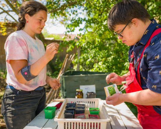 Ein Teilnehmer  von "zusammen wachsen - ökologischer Gartenbau für Jugendliche und junge Menschen mit Behinderungen"  sortiert Samen zusammen  mit der Anleiterin