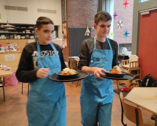 Zwei Teilnehmer von “besser zusammen - Berufsorientierung in der Gastronomie für Jugendliche und junge Menschen mit Behinderungen” bringen  Essen  an einen Tisch