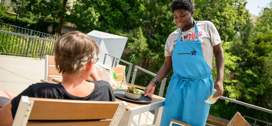 Ein Teilnehmer von  “besser zusammen - Berufsorientierung in der Gastronomie für Jugendliche und junge Menschen mit Behinderungen" bringt einen Salat an den Tisch