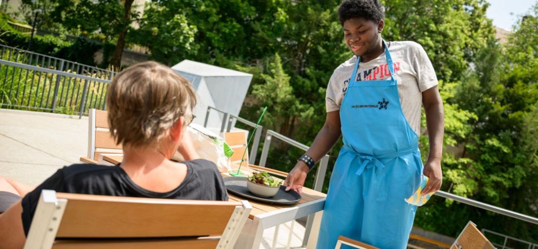 Ein Teilnehmer von  “besser zusammen - Berufsorientierung in der Gastronomie für Jugendliche und junge Menschen mit Behinderungen" bringt einen Salat an den Tisch