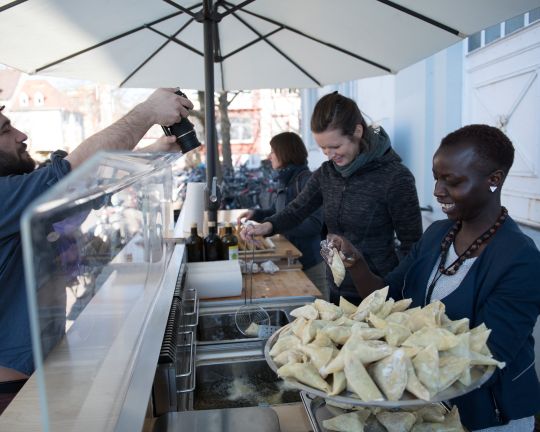Drei Personen verkaufen Samosas an einem Stand.