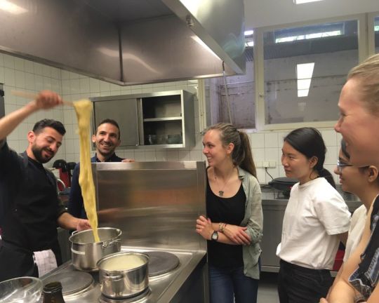 Einige Personen schauen dem Koch zu wie er Essen zubereitet.