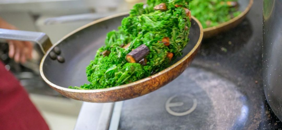 Eine Person schwenkt Gemüse in einer Pfanne.