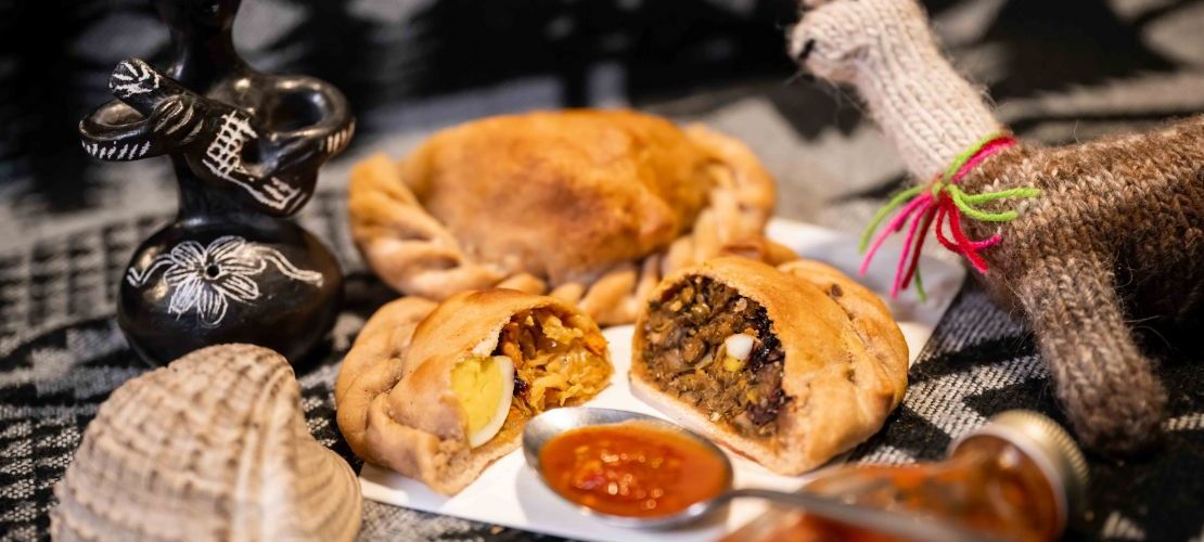 Zweierlei chilenische Empanadas auf einem Teller angerichtet mit Dip. Das sind Teigtaschen aus Weizenmehl gefüllt mit Wirsingkohl oder Linsen.