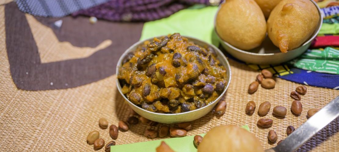 Ein kamerunisches Bohnengericht aus schwarzen Bohnen in einer Schüssel, Beignet, ein fritiertes süßes Hefebällchen und Bouillie, ein Maisgetränk.