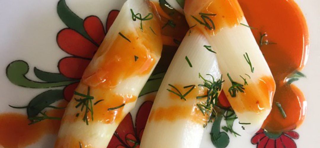 Ein Teller mit weißem Spargel in drei Teile geschnitten und mit roter Soße beträufelt.