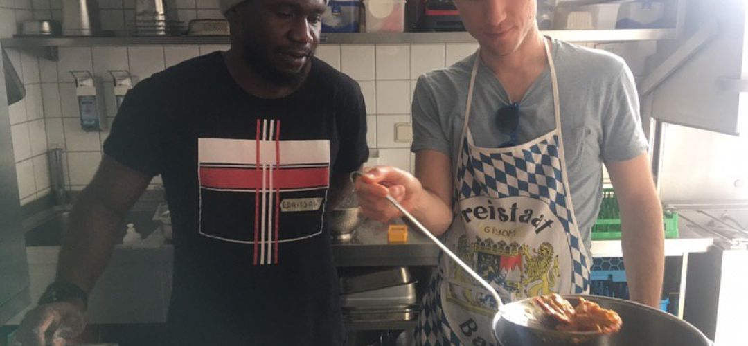 Zwei Personen stehen am Herd vor einem großen Topf und kochen.