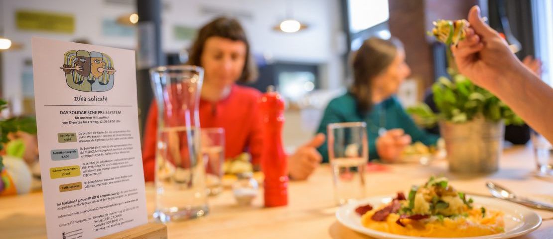 Sozial-ökologischer Mittagstisch beim zuka solicafe: Drei Menschen essen  an einem großen Tisch.