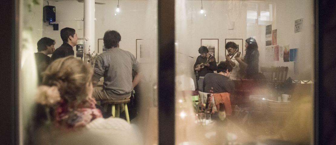 Durch ein beschlagenes fenster sieht man eine  Band und Publikum im Strandcafe bei  "zusammen on stage".