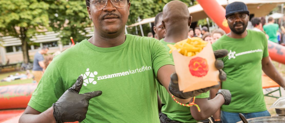 Eine Mann hält eine Schachte Pommes in die Kamera.