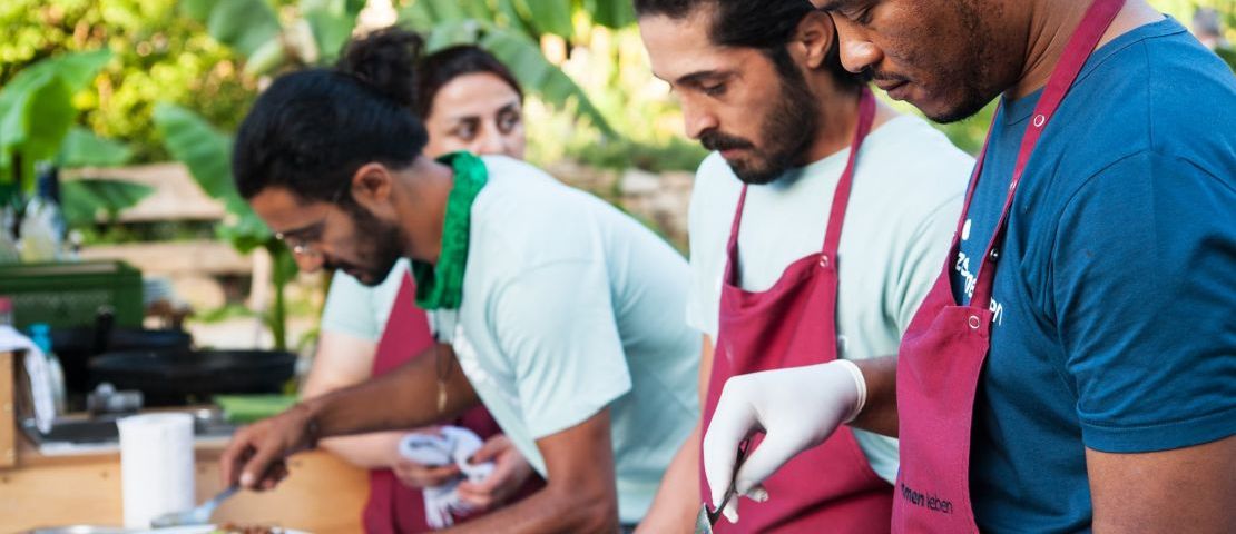 Die Teilnehmer*innen von  "zusammen in die Zukunft,  der BerufsQualifizierung für die Küche, bereiten open air im Gemeinschfatsgarten das Essen für das Eventdinner vor.