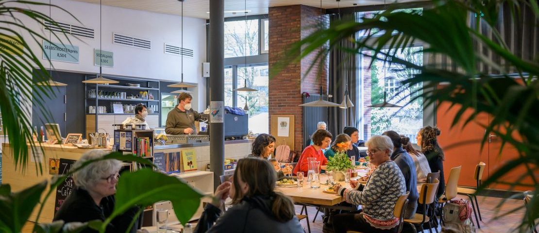 Ein Blick in den Innenraum  des zuka solicafés während des Mittagstisches.  Blick durch die Grünpflanzen.