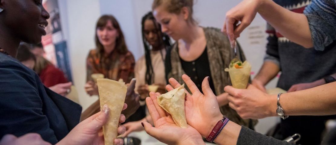 9 junge Menschen stehen um einen Tisch und  befüllen Samosas mitt Gemüsefüllung. Hier wird partizipativ der sozial-ökologische regionale Mittagstisch das erste "Dear  White People" Festival vorbereitet.