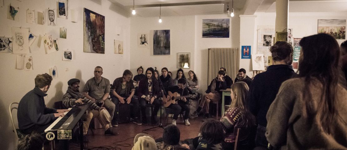 Das Red Moon Collective spielt im Strandcafe bei "zusammen on stage" ein Konzert.  Der Raum ist voll, Menschen sitzen aufdem Boden.