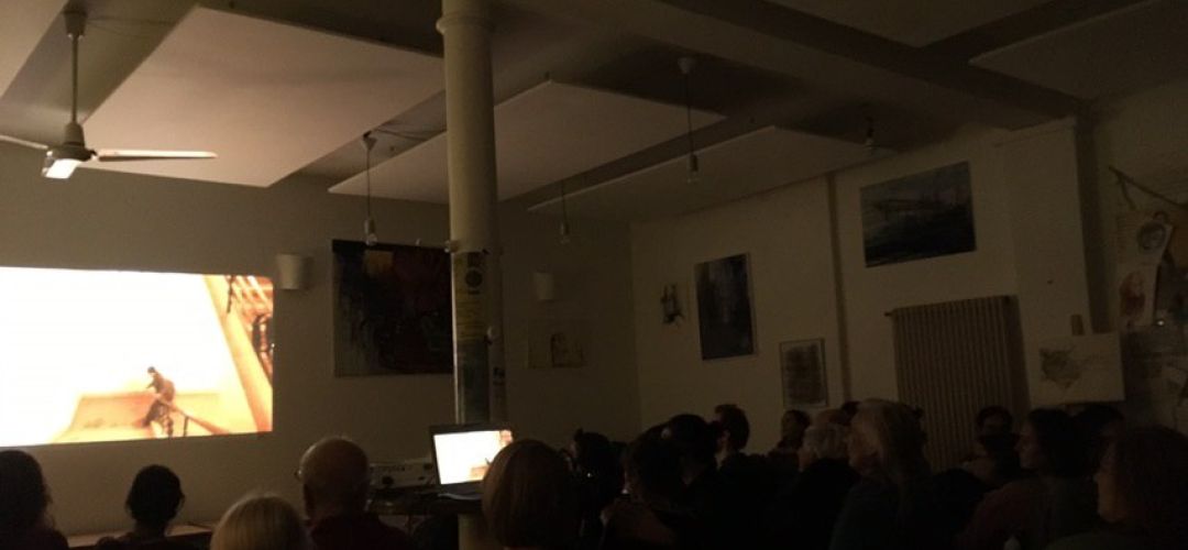 Publikum in einem Saal sitzt vor der Leinwand.