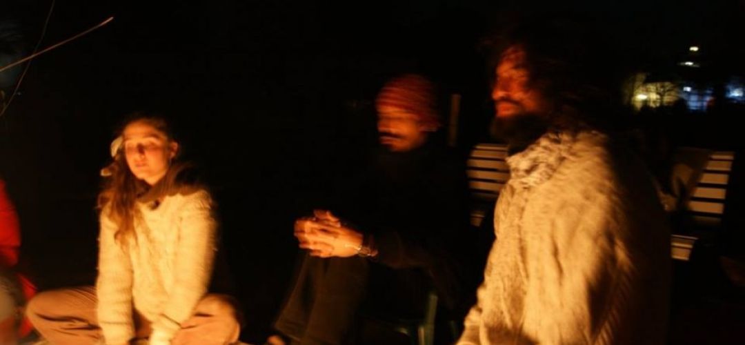 Ein verschwommenes Bild von drei Personen vor einem Lagerfeuer bei Nacht.